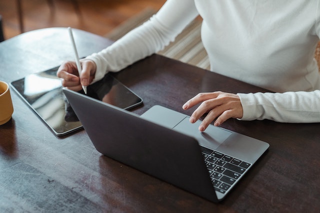 person writing on tablet and typing on computer